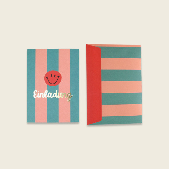 Ava & Yves Einladungskarte im Smiley-Streifen-Design mit goldener Schrift Einladung, daneben passender gestreifter Umschlag.