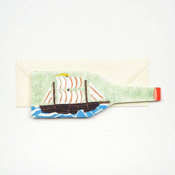 Karte in Flaschenform mit Segelschiff im Mid-Century-Stil; 23 × 7,5 cm, 300-g/m² Karton, elfenbeinfarbener Umschlag im Hintergrund.