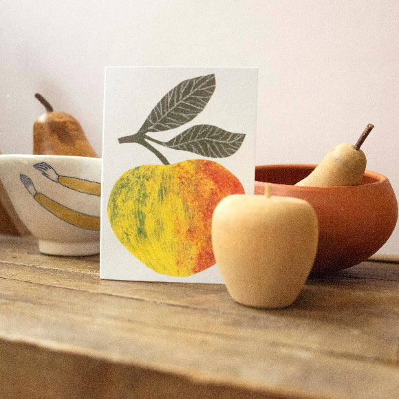 Minimalistische Grußkarte mit gelb-rotem Apfel und grünen Blättern; 10,5 × 7,5 cm auf 300-g/m² Karton, grauer Umschlag im Hintergrund
