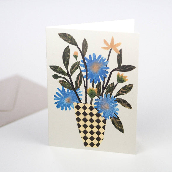 Grußkarte mit blauem Wildblumenstrauß in schwarz-beiger Karo-Vase auf hellem Hintergrund; grauer Umschlag dahinter