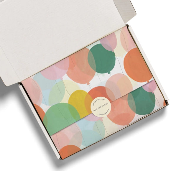 Bunt bedrucktes Seidenpapier mit Ballonmotiv, dekorativ in einer Versandbox arrangiert.